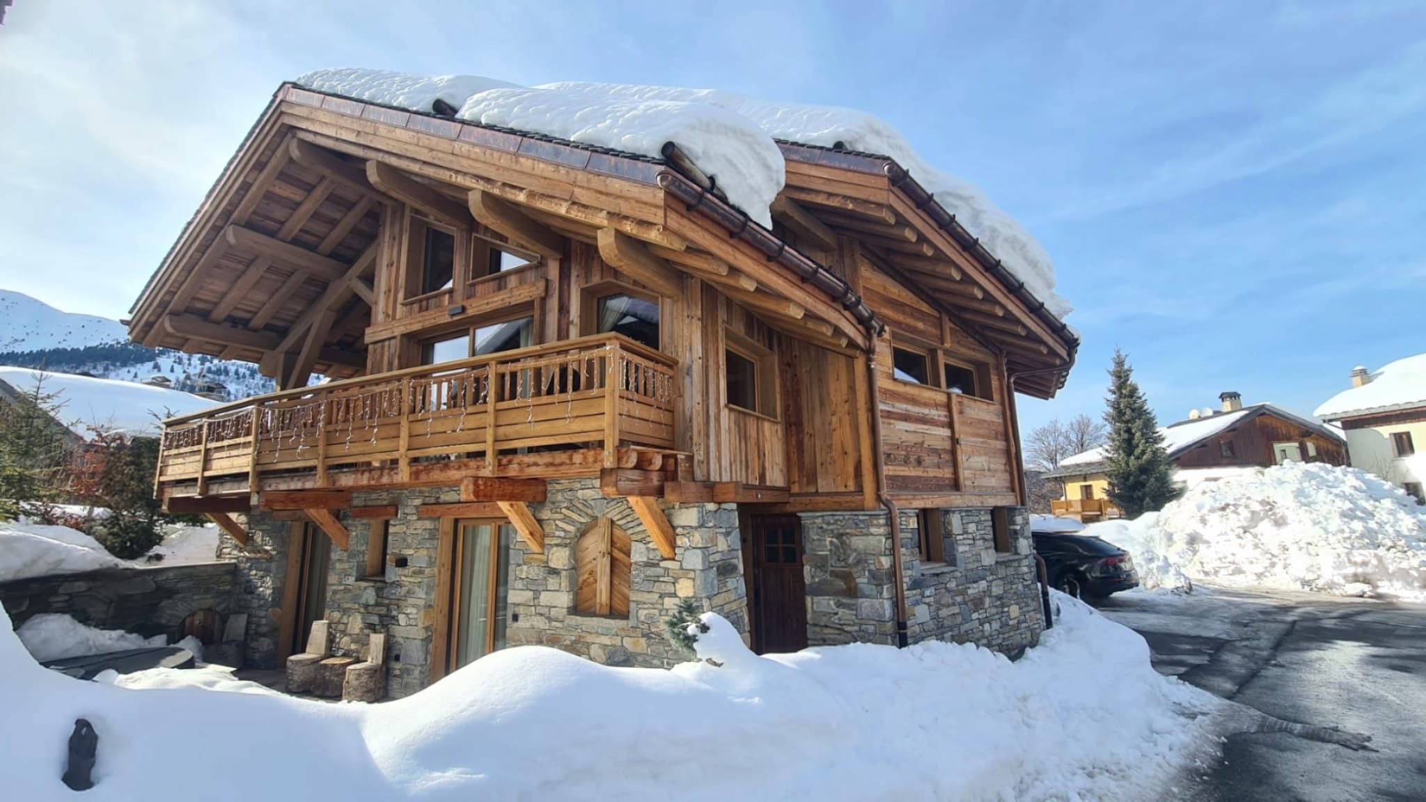 The chalet in deep snow under a blue sky, with its timber balcony and stone base